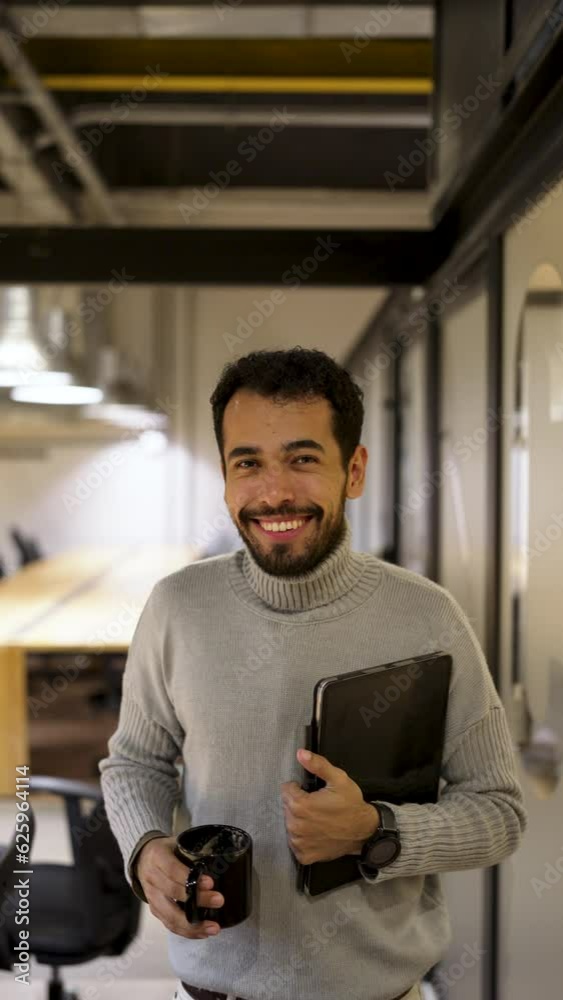 close up portrait young adult Latin American business man standing and holding a tablet and coffee cup indoors