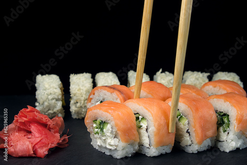 Sushi Rolls on a black background. Chopsticks take a roll. Traditional Japanese Cuisine