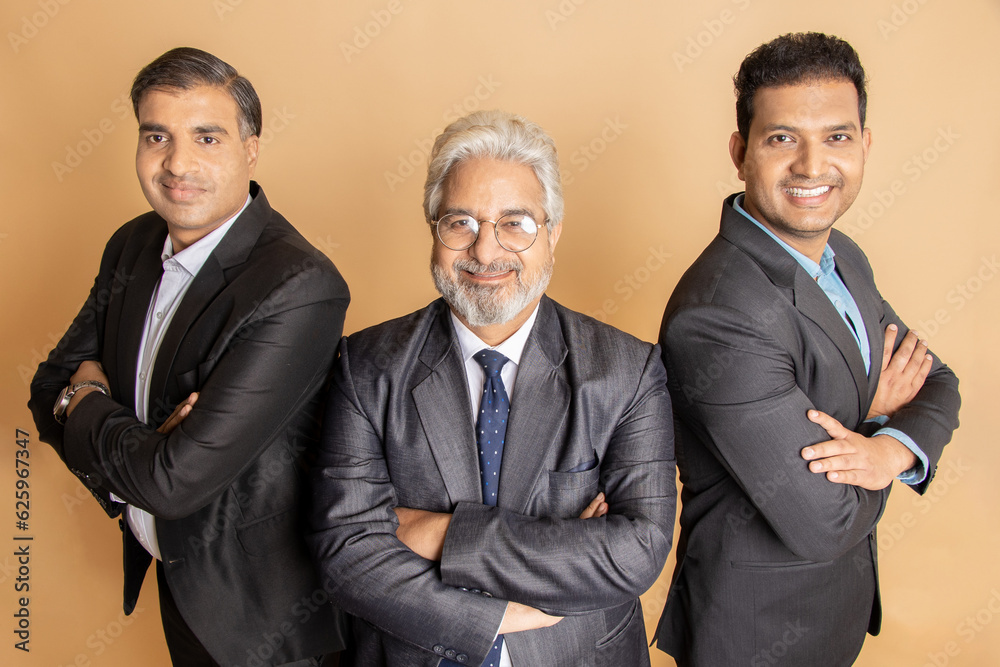 Group of positive indian businessmen wearing suit standing cross arms looking at camera with smiles isolated on beige studio background. corporate people. Group of positive indian businessmen wearing suit standing cross arms looking at camera with smiles isolated on beige studio background. corporate people.