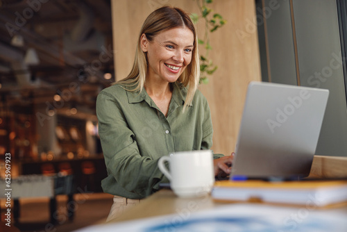 Smiling woman entrepreneur working on laptop in modern coworking. Distance work concept