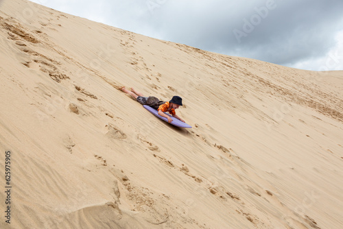 A young boy is having great fun on an adventure activity in New Zealand called sand boarding. He is sliding dow a large sand dune. 