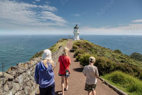 A mum and two children are walking away from the camera towards Cape Reinga lighthouse, which is at the far north of the North Island in New Zealand.