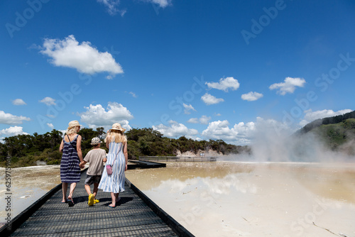 A mum and two children are visiting Wai-o-tapu geothermal reserve in New Zealand. Full of hot springs, mud pools and colourful mineral deposits, this is a huge tourist attraction.  photo