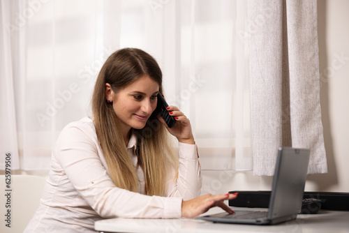 A girl at the office with the laptop talking on the phone and smiling 