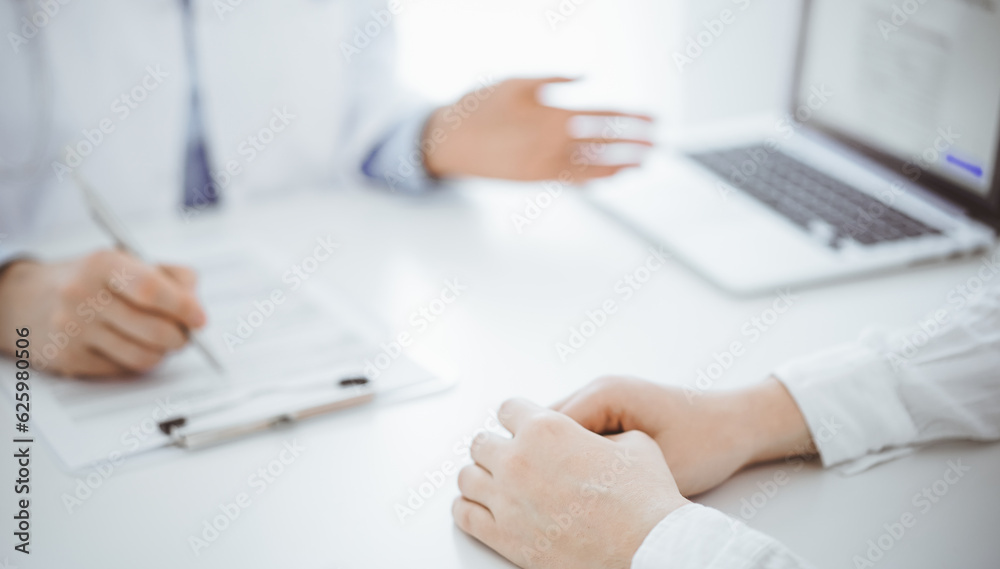 Doctor and patient using tablet computer while sitting opposite each other at the desk in clinic. The focus is on female hands near physician, close up. Medicine concept Doctor and patient using tablet computer while sitting opposite each other at the desk in clinic. The focus is on female hands near physician, close up. Medicine concept