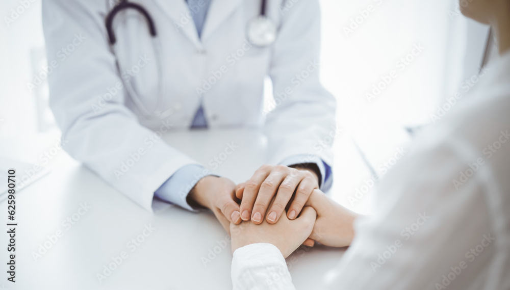 Doctor and patient sitting opposite each other at the table in clinic office. The focus is on female physician's hands reassuring woman, only hands, close up. Medicine concept Doctor and patient sitting opposite each other at the table in clinic office. The focus is on female physician's hands reassuring woman, only hands, close up. Medicine concept