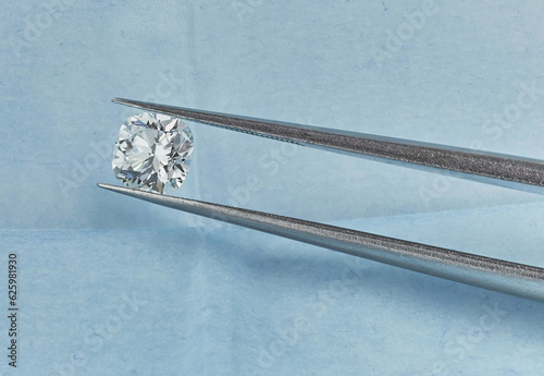Cushion Cut Diamond. Macro Diamond Photograph of Fancy Cushion Diamond in Blue Parcel Background with Tweezers. 