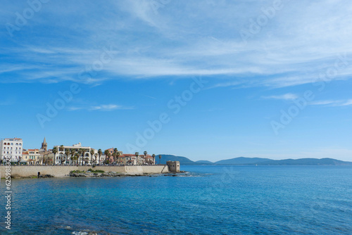 Panorama of coast of Alghero in spring Sardinia, Italy. Alghero cityscape seen from far under vibrant clear blue sky