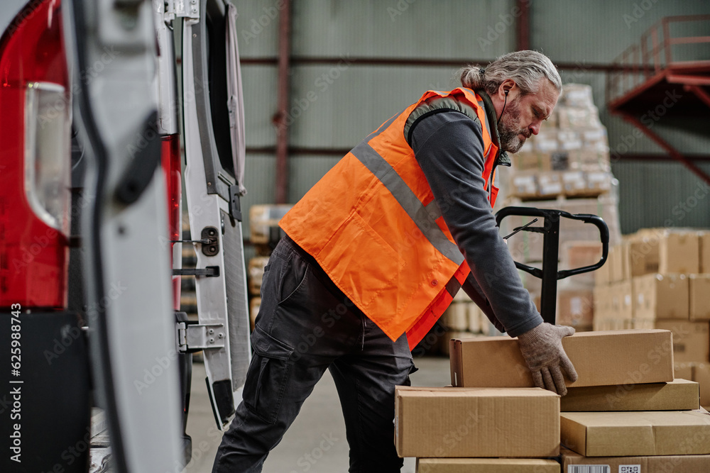 Mature worker loading cardboard containers in truck during his work in warehouse Mature worker loading cardboard containers in truck during his work in warehouse
