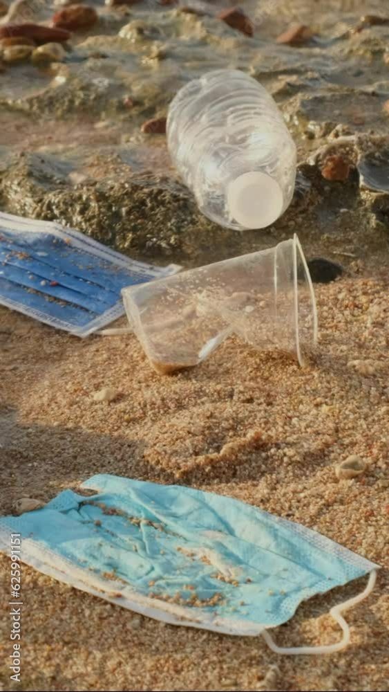 VERTICAL VIDEO, Close-up of disposable plastic, face mask and other debris on corals beach in surf zone. Plastic and other garbage on the seashore. Slow motion VERTICAL VIDEO, Close-up of disposable plastic, face mask and other debris on corals beach in surf zone. Plastic and other garbage on the seashore. Slow motion