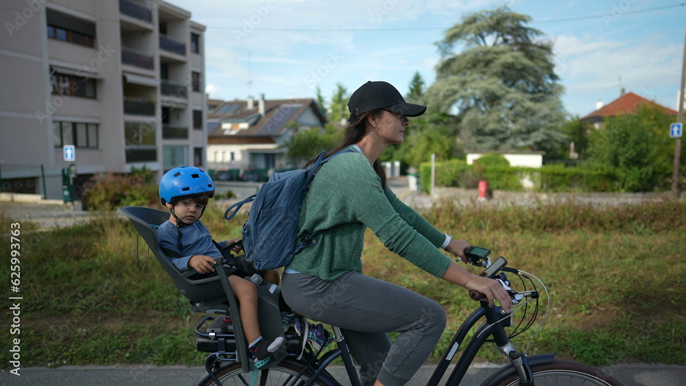 Mother riding bicycle with child in back seat outside in urban green path