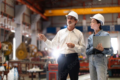 two professional engineer,worker,technician use clipboard discuss work, walk in steel metal manufacture factory plant industry. Black African American man and woman wear hard hat check quality machine photo