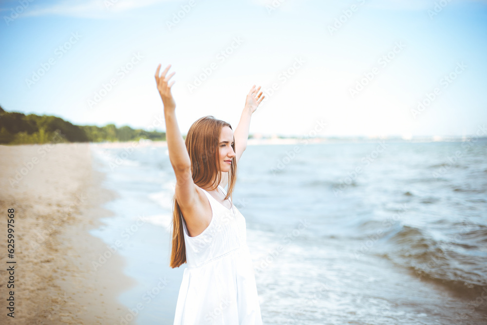 Happy smiling woman in free happiness bliss on ocean beach standing with raising hands. Portrait of a multicultural female model in white summer dress enjoying nature during travel holidays vacation Happy smiling woman in free happiness bliss on ocean beach standing with raising hands. Portrait of a multicultural female model in white summer dress enjoying nature during travel holidays vacation