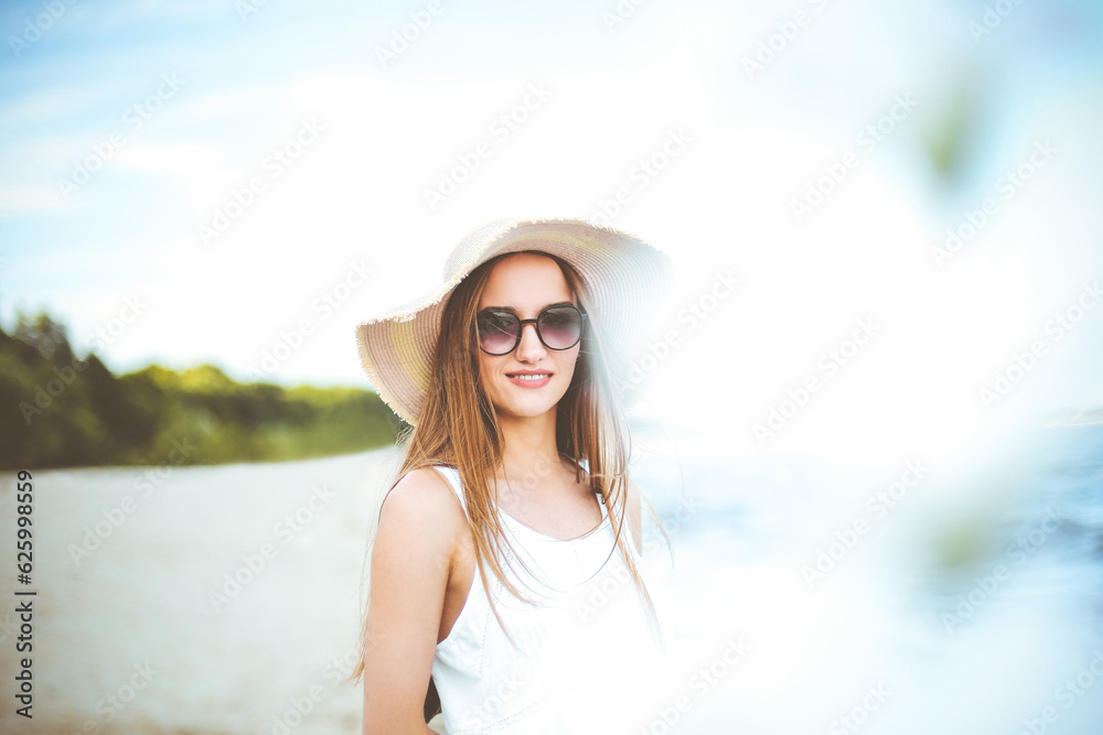 Happy smiling woman in free happiness bliss on ocean beach standing with hat, sunglasses, and white flowers. Portrait of a multicultural female model in white summer dress enjoying nature during
