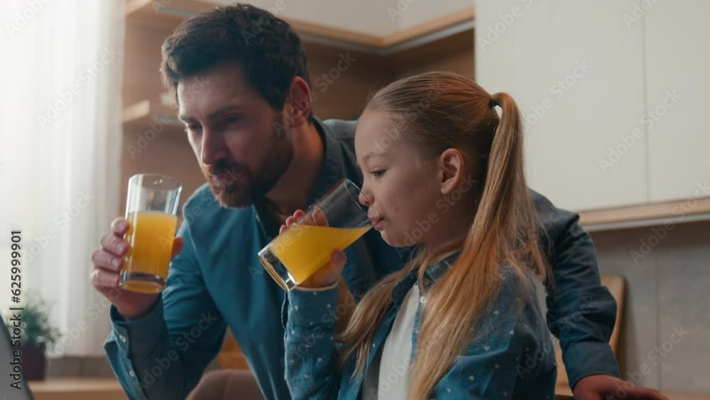 Caucasian happy family at kitchen adult father with little daughter child girl drinking fresh drink tasty orange juice looking at laptop dad teach using computer technology kid help with e-learning