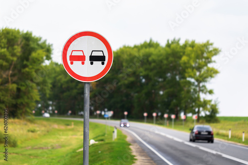 The overtaking sign is prohibited on the background of a highway with passing cars
