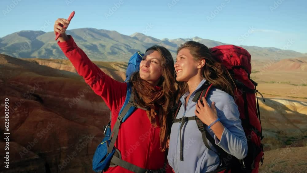 Two young woman traveler using mobile phone taking selfie while travel on mountain in autumn sunny day. Attractive girls enjoy outdoor lifestyle in holiday vacation trip. Two young woman traveler using mobile phone taking selfie while travel on mountain in autumn sunny day. Attractive girls enjoy outdoor lifestyle in holiday vacation trip.