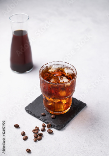 Cold brew coffee in a glass with ice on a light background with coffee beans and bottle. Concept summer craft refreshing homemade drink.