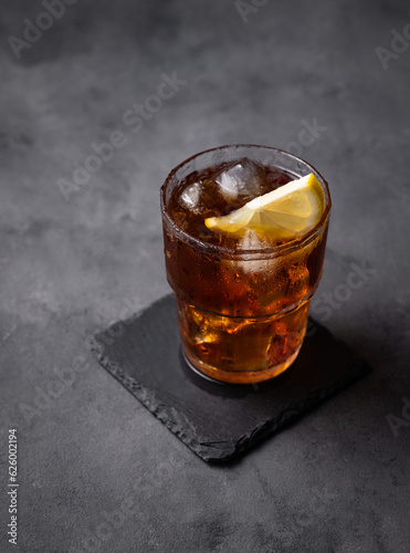 Iced tea, Cuba Libre or Long Island cocktail with cola, lemon and ice in a glass on a dark background. The concept of a cold refreshing drink or lemonade.