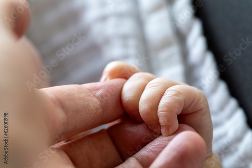 A close up portrait of the small tiny fingers of a baby grabbing or clutching the fingers of the hand of the parent. Showing the love, dependency and care between a child and parent.