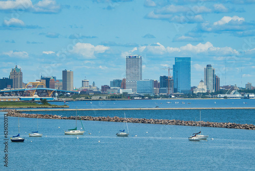 On a sunny Summer day, the view of Downtown Milwaukee as seen from beyond a harbor with a few boats.