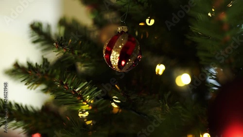  Female hand decorates a christmas tree with small red ball
