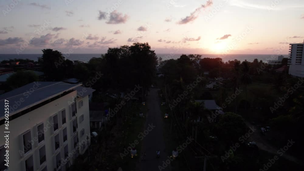 Water tower at sunset with a view of Phuket Island. Orange sun, sea and clouds. Around the tower there are green palm trees, hotels and swimming pools. People are bathing. Karon, passing transport Water tower at sunset with a view of Phuket Island. Orange sun, sea and clouds. Around the tower there are green palm trees, hotels and swimming pools. People are bathing. Karon, passing transport