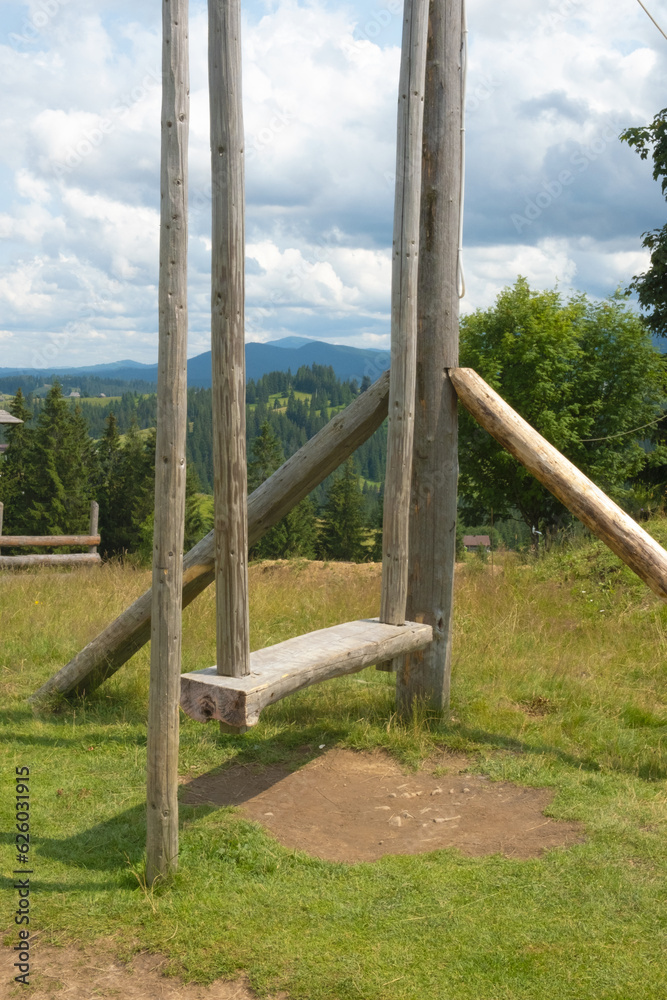 A wooden swing for sitting and enjoying the mountain view in the cloudy summer day.