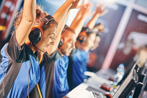 Side view of a excited mixed race girl, female cybersport gamer raising hands up, celebrating success with her team, participating in esports tournament