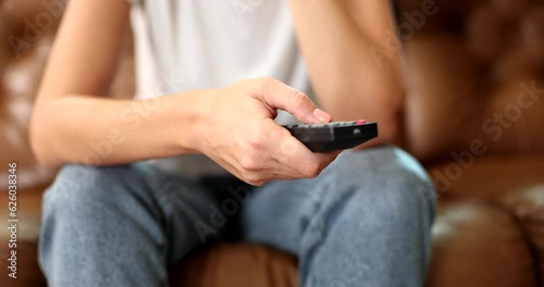 A woman sitting at home on the couch presses the remote control button, a close-up. Pasive rest, relaxation photo