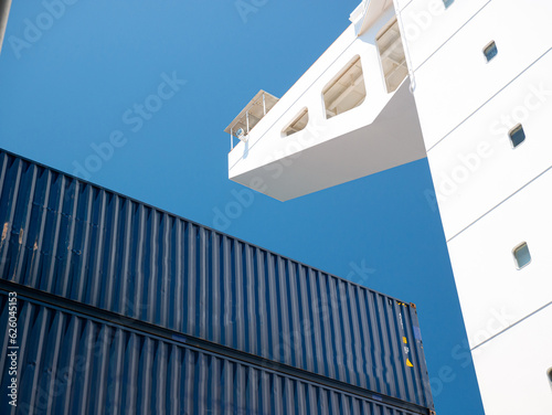 Side wing of navigational bridge and and blue containers stored on deck of ultra large containers ship