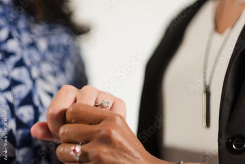 A multiracial lesbian couple holds hands and shows off their engagement rings, celebrating their love.