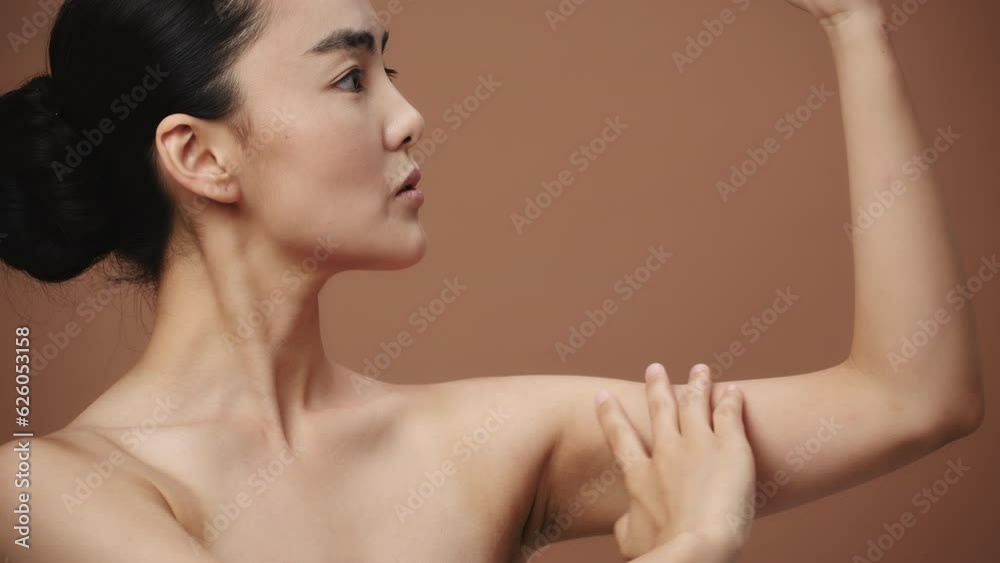 Close-up of a beauty asian young woman touches her soft skin on her bicep, on a beige background. Beautiful female model with perfect clean fresh skin. Skin care treatment concept