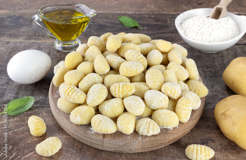 Uncooked italian potato gnocchi and cooking ingredients on wooden background. photo