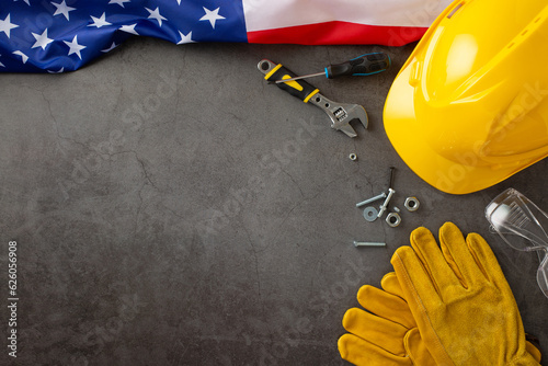 Paying tribute to invaluable contributions of construction workers on American Labor Day. Above photo of flag, helmet, gloves and equipment on grunge textured grey concrete. Perfect for ads or text