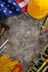 Recognizing the hard work and dedication of construction workers on Labor Day. Top vertical image showcasing flag, helmet, gloves, and tools on grunge textured grey concrete. Copyspace for ads or text