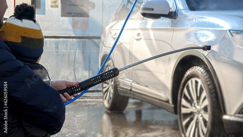 Closeup of man with baby boy washing car at carwash with water jet. Automobile care, transport cleaning, dirty car.