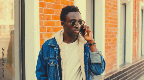 Portrait of stylish african young man talking on phone while walking on city street