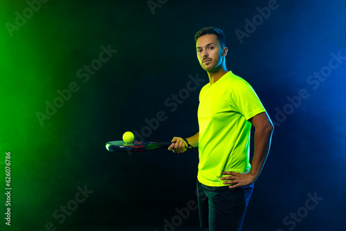 Padel tennis player celebrates victory in the game. Man athlete with paddle tenis racket on blue background. Sport concept. Download a high quality photo for sports website. © Mike Orlov