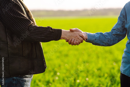 Two farm owners shake hands on a green field. Successful deal. Agriculture and business concept.