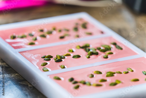 Pink chocolate bars in moulds. Ruby chocolate production process. Modern chocoat with pistachios. Chocolate moulds isolated on brown kitchen counter. High quality photo