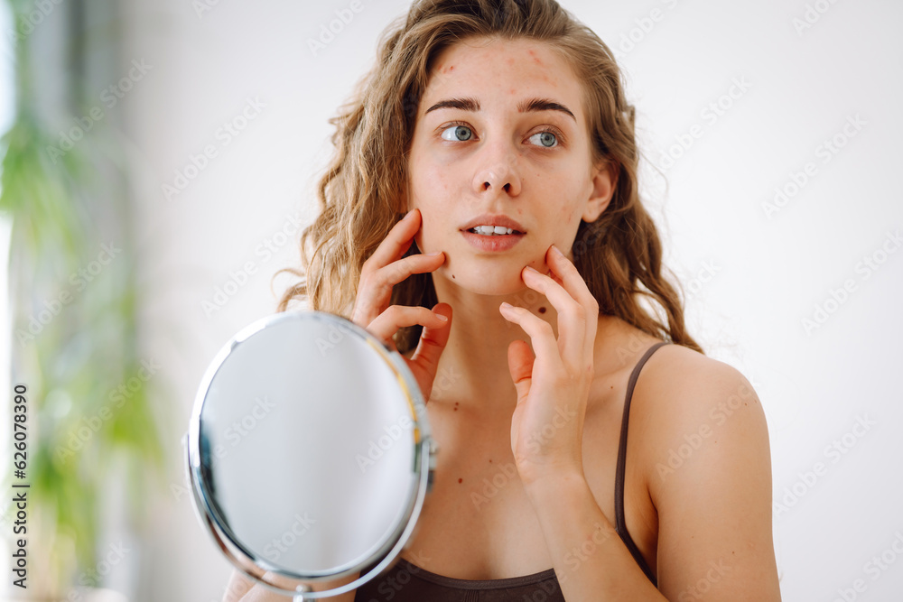 Skin problem. Curly woman touches red inflammations on her face while looking in the mirror in a bright room. Facial skin problems. Beauty care. Allergic reaction. Skin problem. Curly woman touches red inflammations on her face while looking in the mirror in a bright room. Facial skin problems. Beauty care. Allergic reaction.
