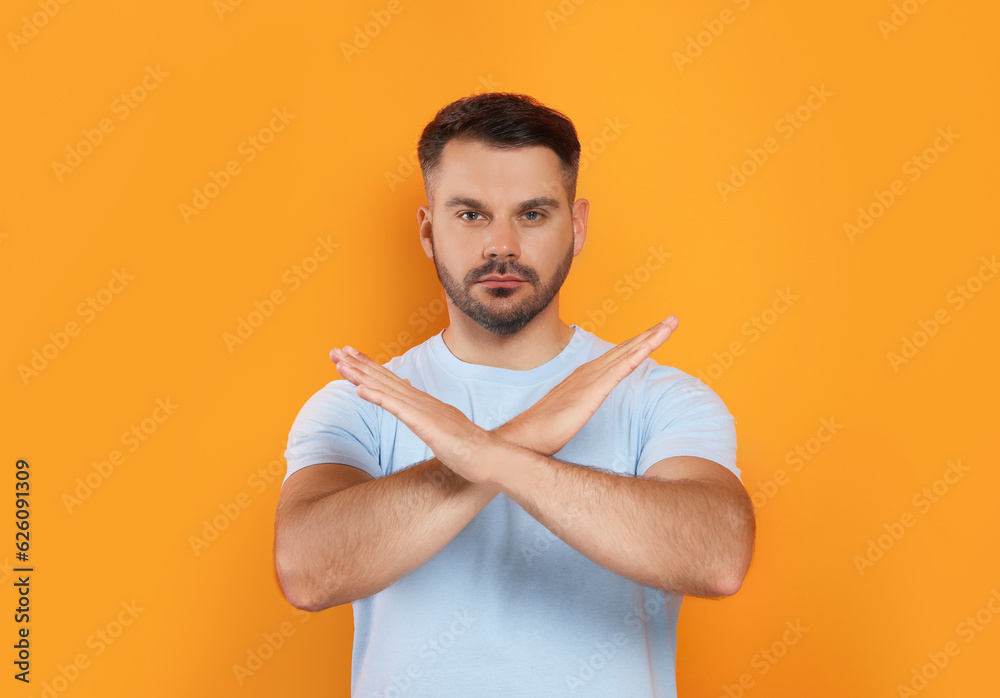 Handsome man with crossed hands on orange background. Stop gesture Handsome man with crossed hands on orange background. Stop gesture