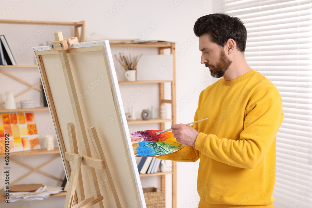 Man painting in studio. Using easel to hold canvas Man painting in studio. Using easel to hold canvas
