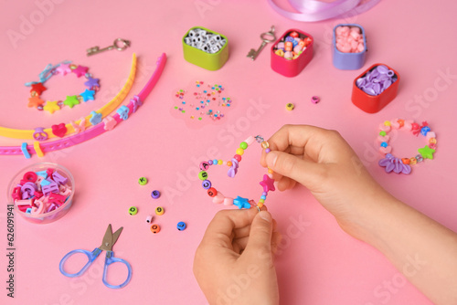 Child making beaded jewelry and different supplies on pink background, above view. Handmade accessories