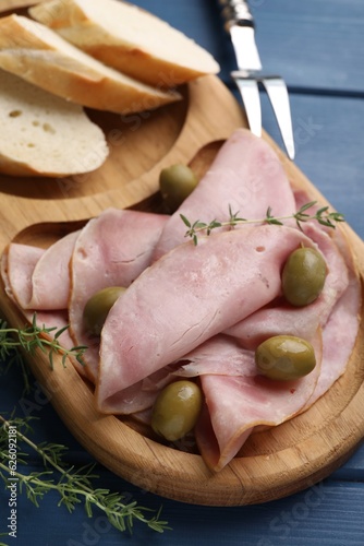 Slices of delicious ham with olives and baguette served on blue wooden table, closeup