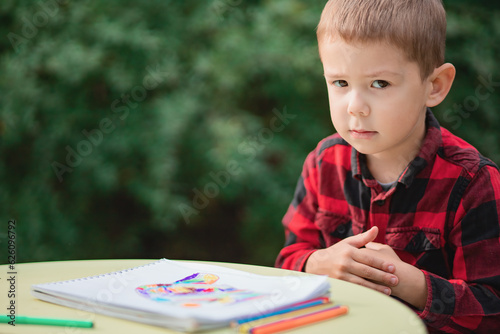 Child not happy with his drawing,  looks into the camera. Outdoors kids portrait, copy space. photo