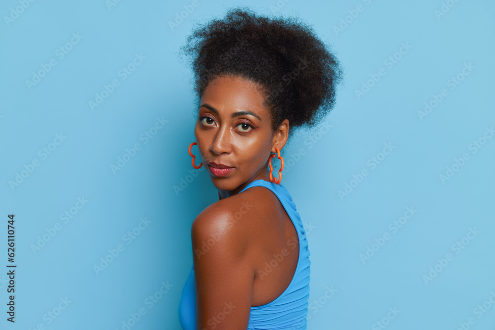 Close-up face to shoulder of beautiful coloured girl in blue top on blue background, serious look into camera, natural beauty concept, copy space Close-up face to shoulder of beautiful coloured girl in blue top on blue background, serious look into camera, natural beauty concept, copy space
