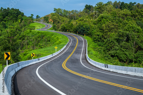 Long curvy forest asphalt road over the hills. Beautiful curved road in the forest. Side view of road. © yotrakbutda