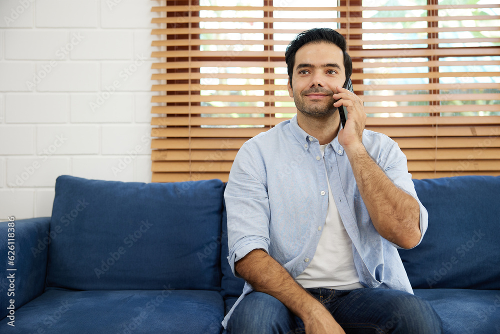young handsome man sitting on sofa and talking by smartphone at home